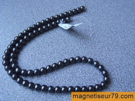 Collier de perles noires enfilées sur un support gris.