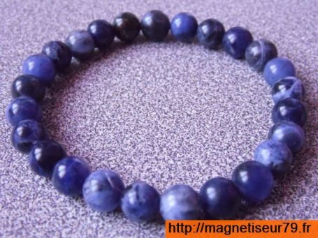 Bracelet en perles de pierre bleue, sphériques et régulières sur fond gris.